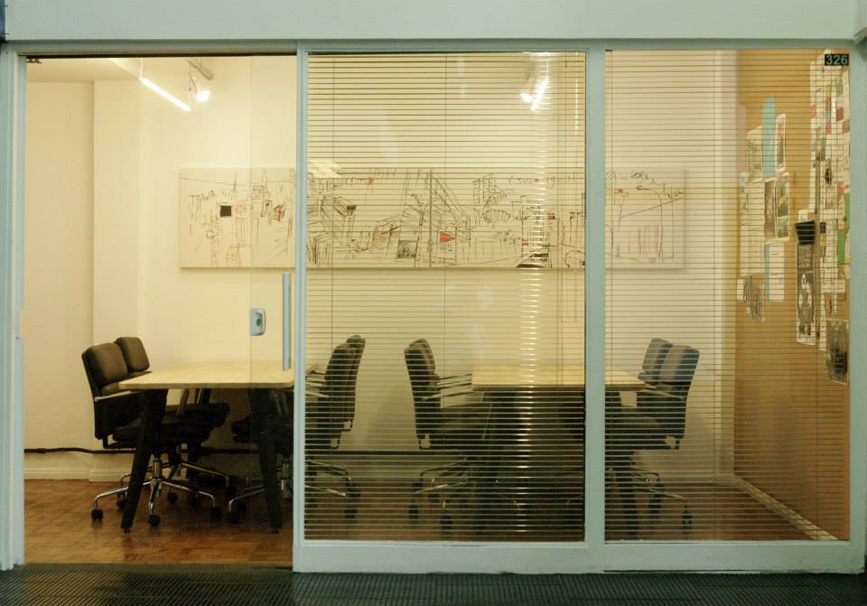 Photo of the InternetLab office, where there is a sliding glass door, two white tables with four black chairs on each. On the wall, there is a white, black and orange painting of downtown São Paulo.