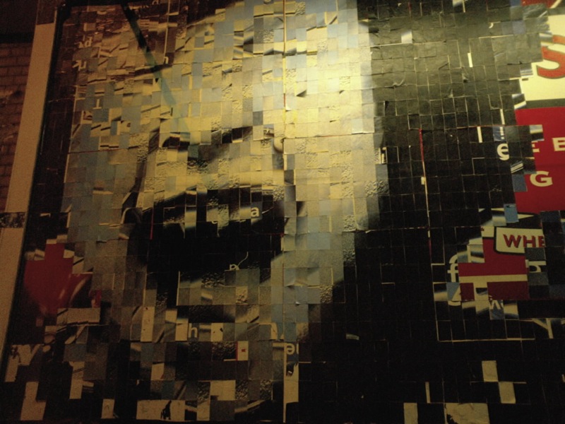 Photo of a black and white collage made on a wall that forms the image of a screaming child's face, with eyes closed and mouth open