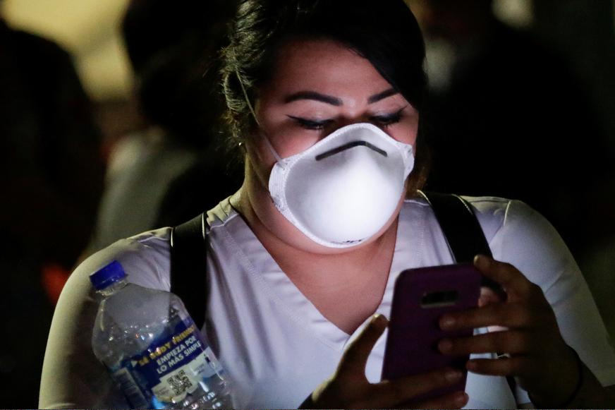 Foto de mulher branca com máscara respiratória usando o celular