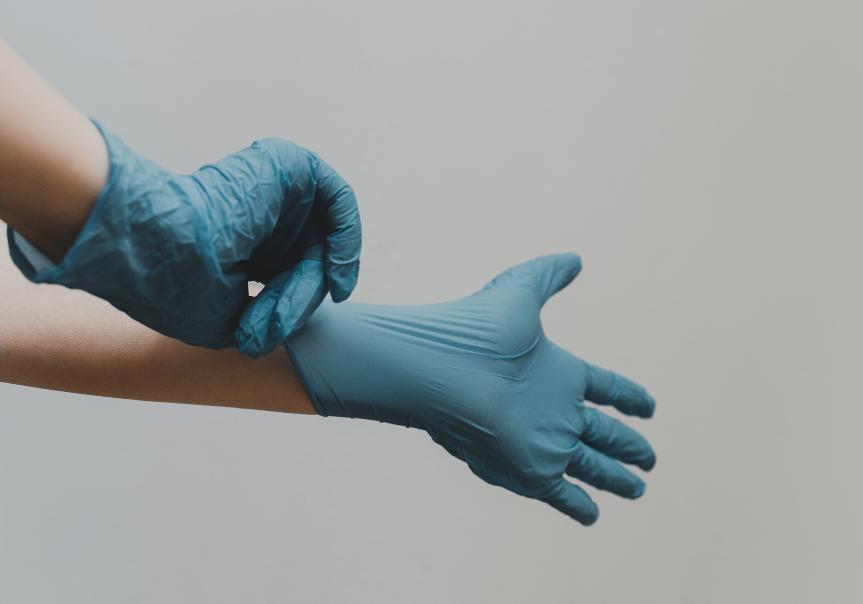 Imagem ilustrativa de pessoa branca colocando luvas cirúrgicas azuis.